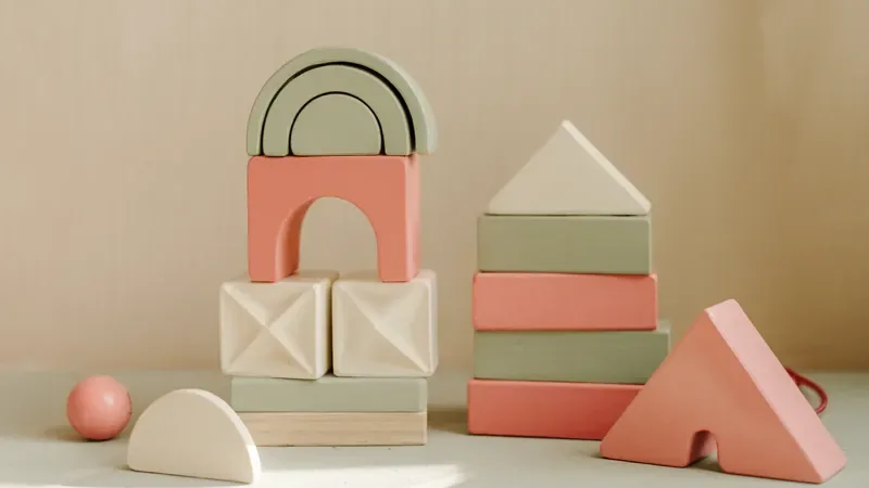 Blocos de madeira em creme, verde-sálvia e coral empilhados sobre mesa clara