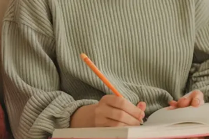 Adolescente de suéter escrevendo a lápis em um caderno aberto